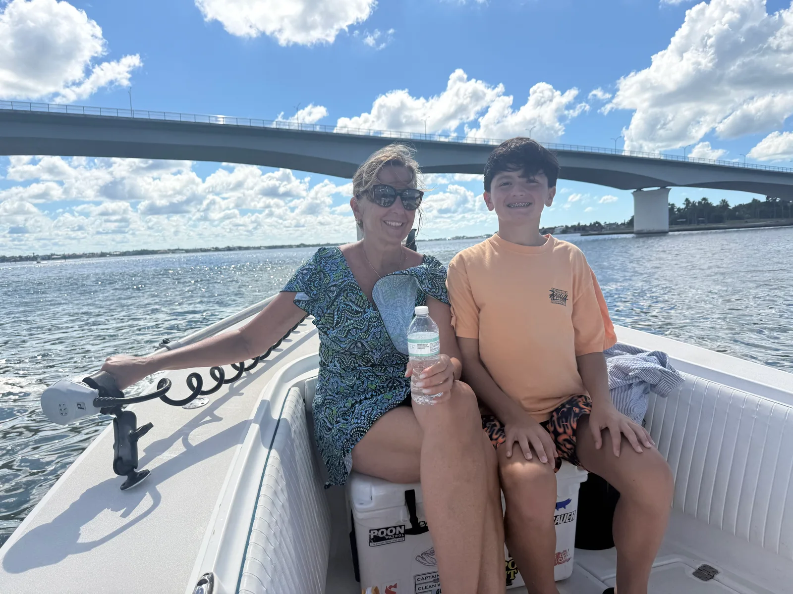 Adult and young angler sit aboard a boat beneath a bridge during a Sarasota fishing trip — October 15, 2026.
